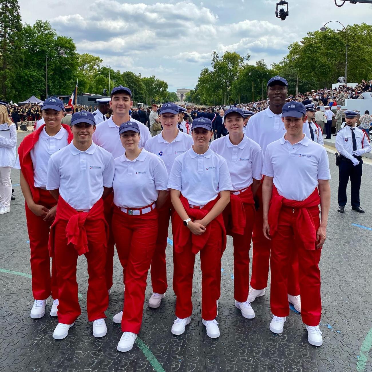 Grupo de jóvenes con pantalón rojo y camisa blanca participando en el desfile del 14 de julio en París